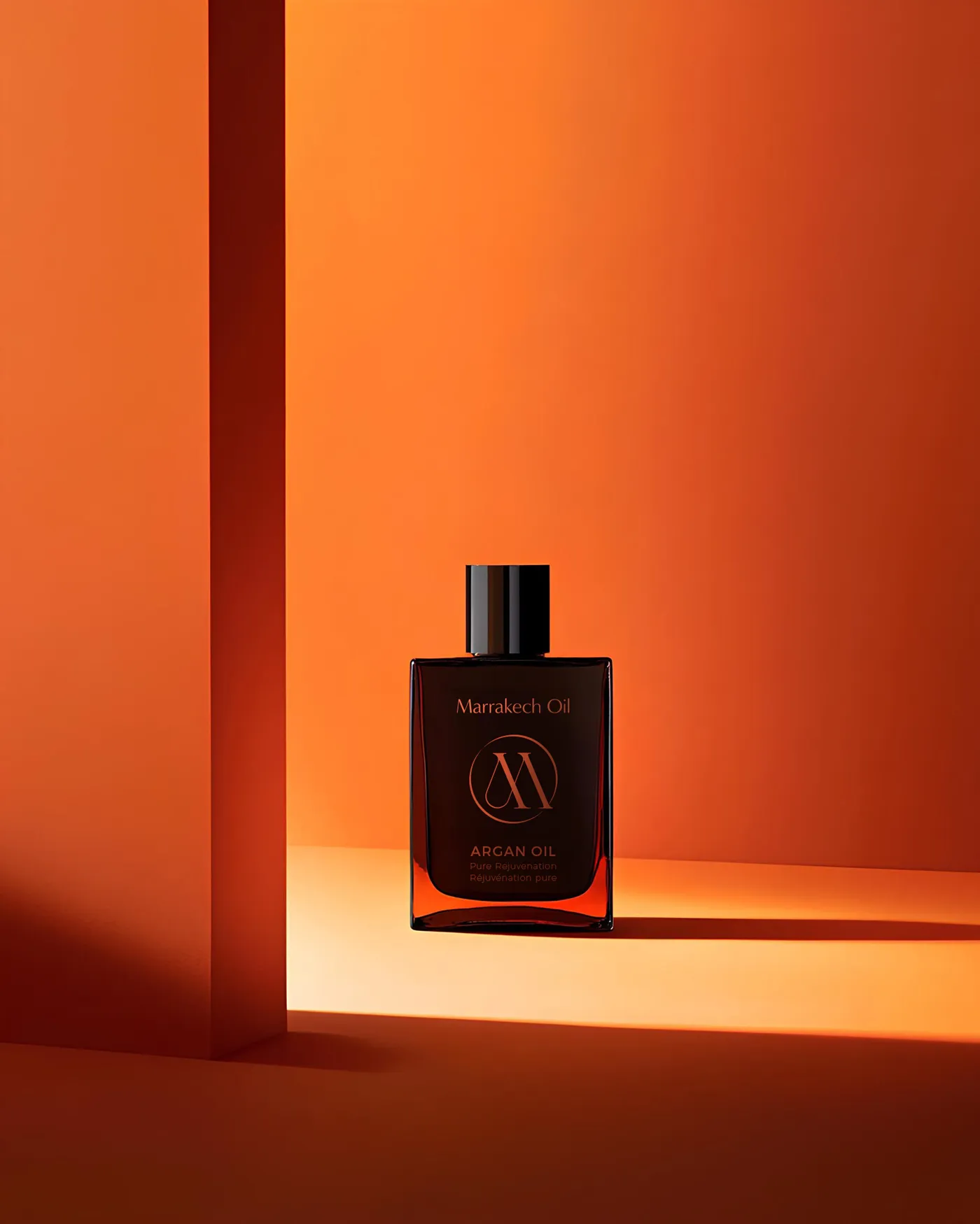 A modern product shot of Marrakech Oil's Argan Oil in a dark, square bottle against a vibrant orange backdrop, showcasing bold beauty branding.