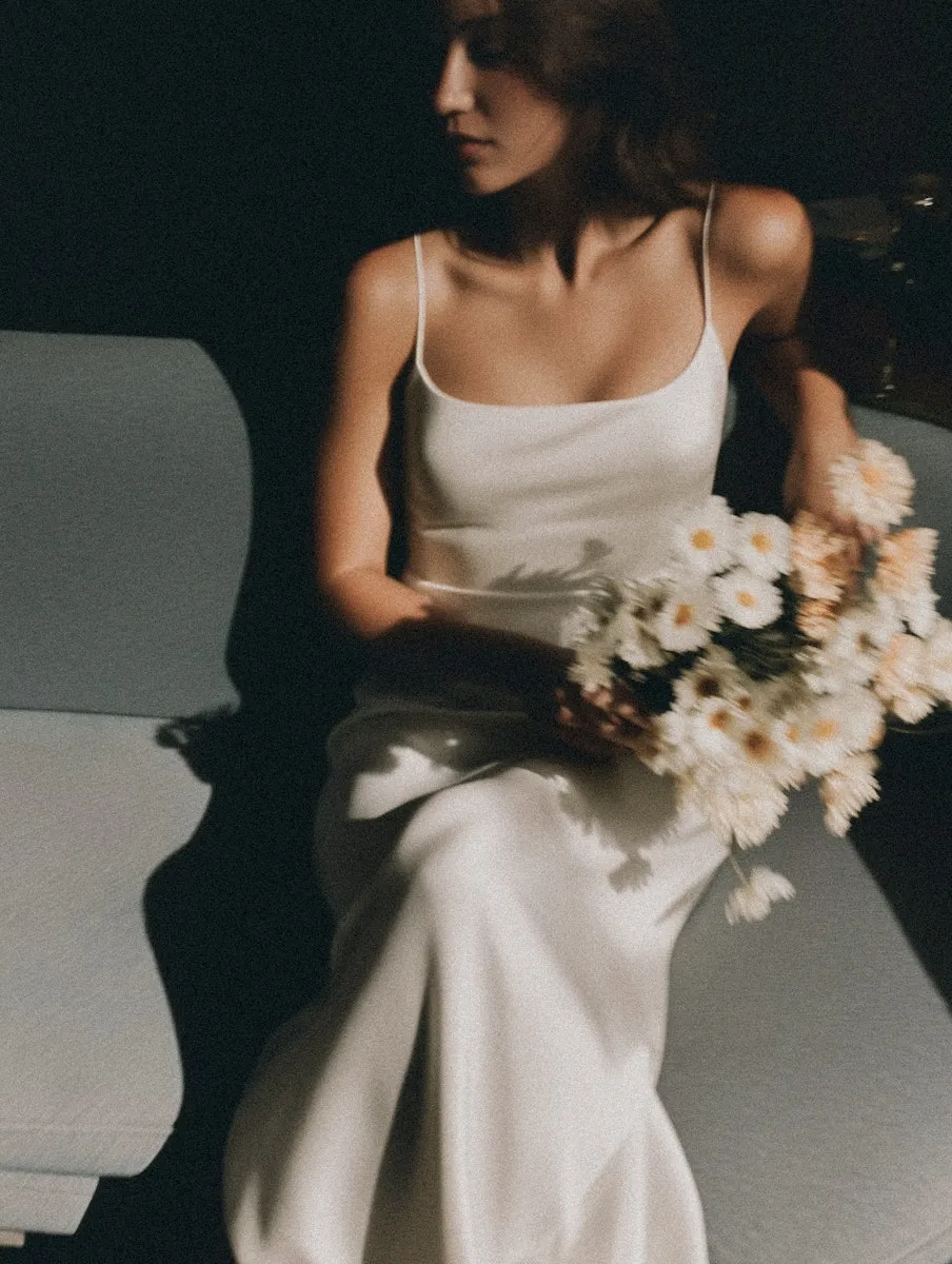 An atmospheric lifestyle shot for the Marrakech Oil brand, featuring a model in a silk dress holding a bouquet of flowers to evoke a sense of natural beauty.